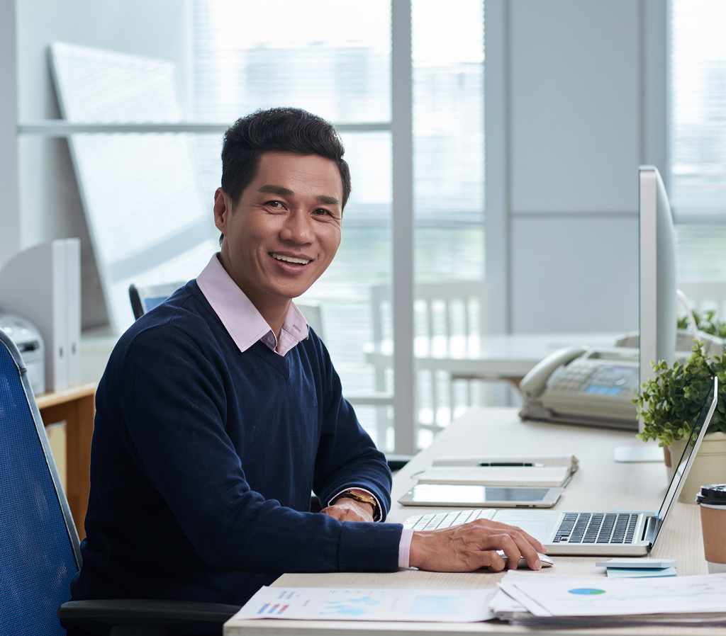 Smiling Vietnamese businessman sitting at an office desk looking at the camera